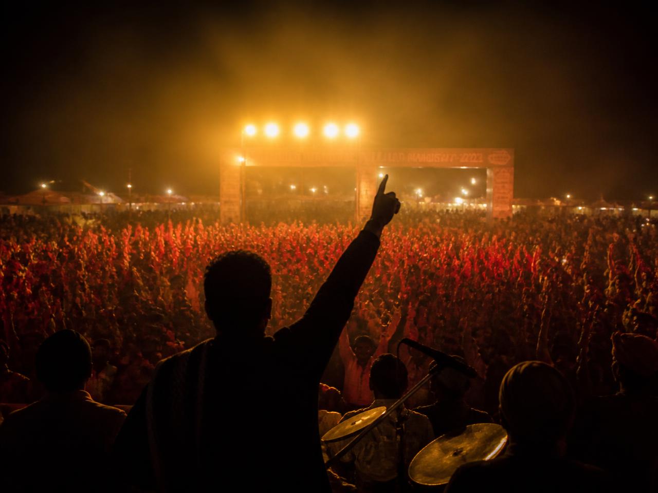 Festival audience at night with raised hands lit by warm golden stage lights