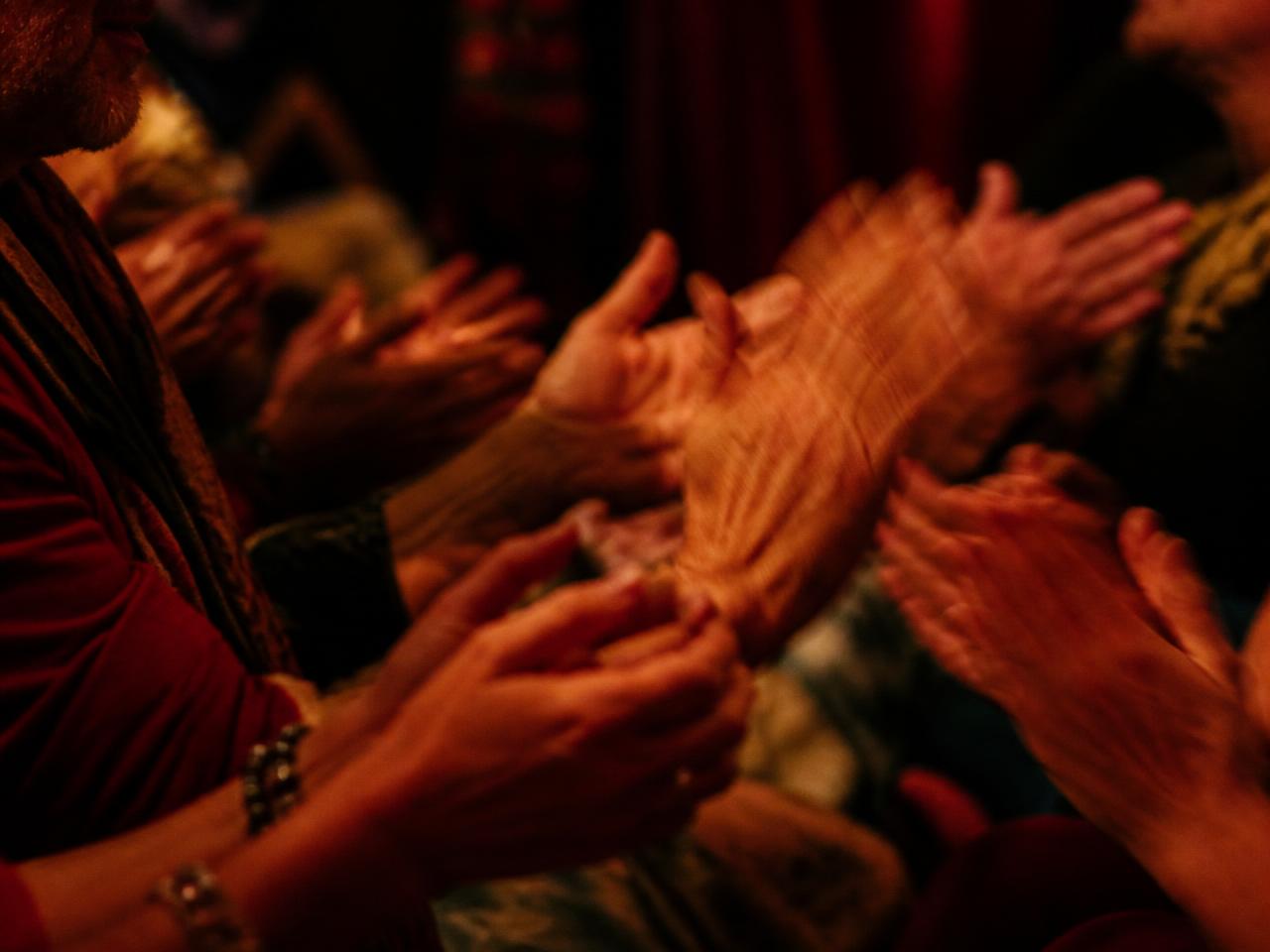 Close view of many hands clapping together in warm low light during a rhythm workshop