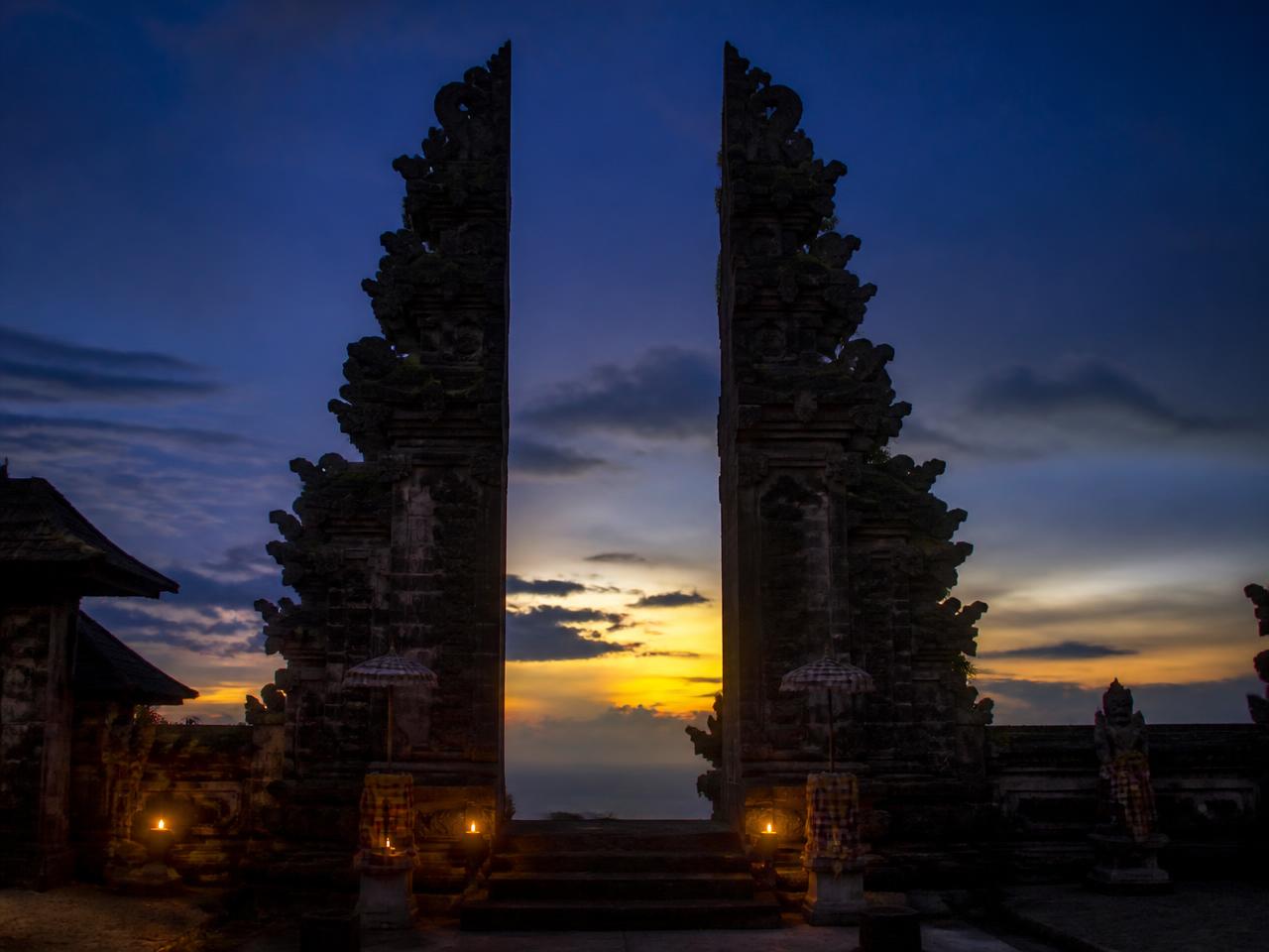 Silhouetted Balinese split temple gateway at dusk with oil lamps glowing on the steps